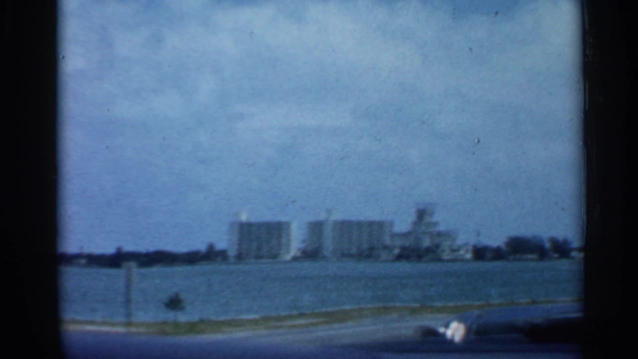 Distant waterfront buildings seen across water from a moving car window.