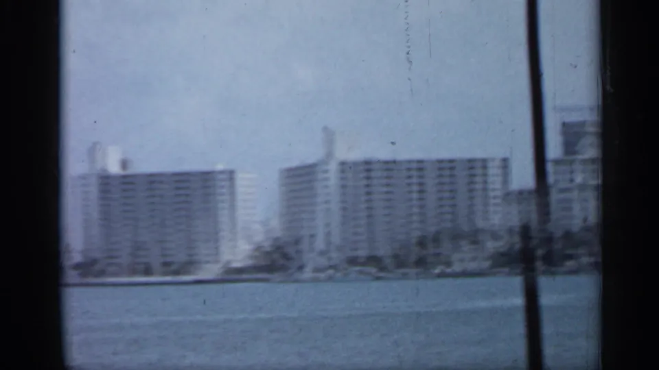 Florida waterfront buildings across the water, with a dark vertical window or vehicle frame crossing the 8mm home-movie view.