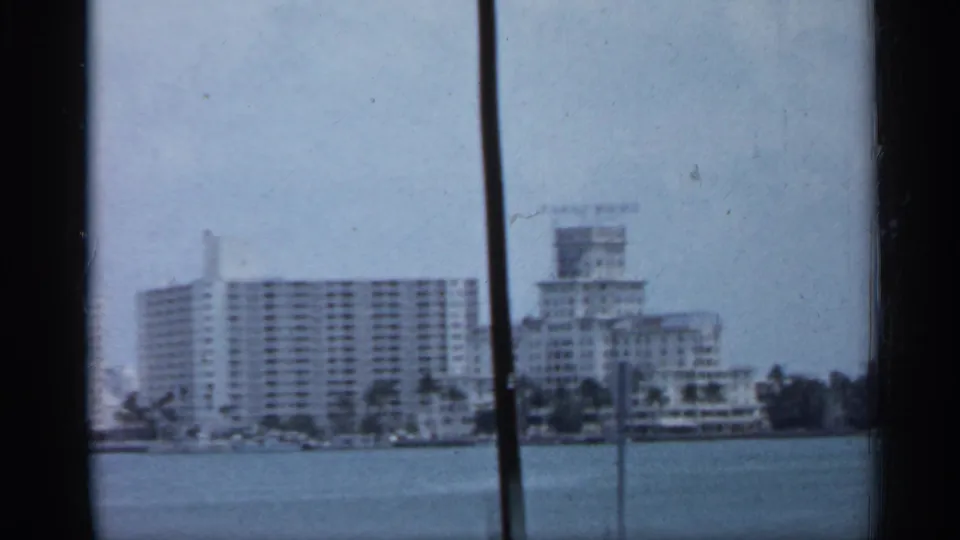 1958 Florida waterfront view with white high-rise buildings across the water, framed by dark film edges and a vertical obstruction.