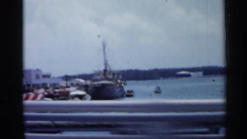 1958 Florida harbor view with boats, parked cars, water, and a low shoreline, partly obscured by motion blur from the moving camera.