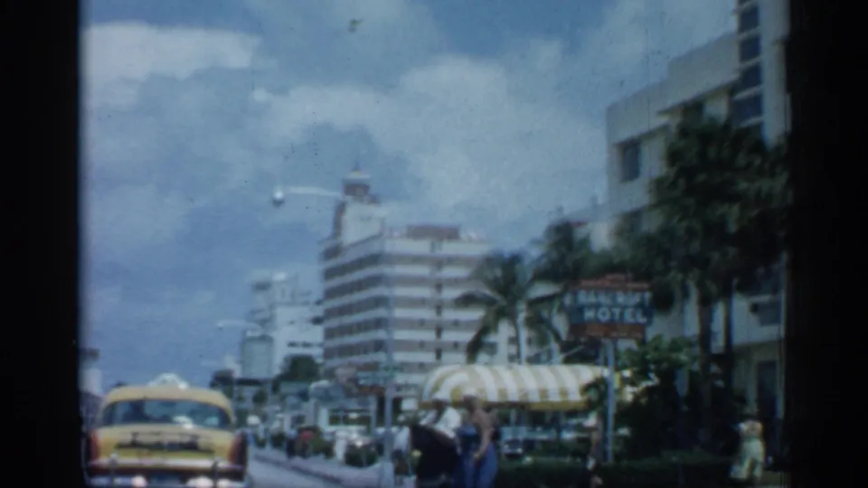 1958 Florida street view with a yellow taxi, pedestrians, palm trees, hotel buildings, and a visible Bancroft Hotel sign.
