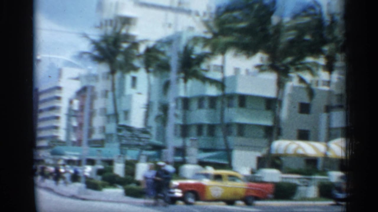 1958 Florida street view with palm trees, low-rise Art Deco-style buildings, pedestrians and a red-and-yellow vehicle in traffic.