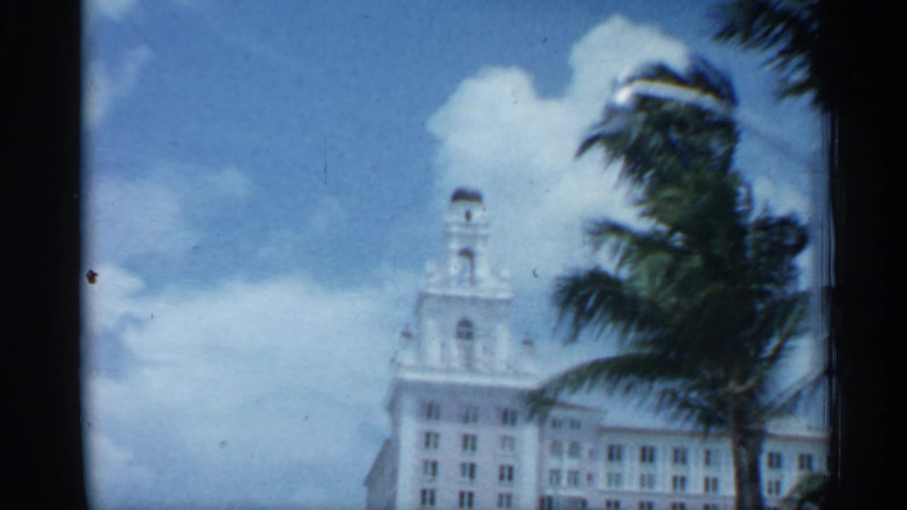 Florida street view showing a white towered building, palm fronds, clouds, and soft 8mm exposure from a moving home-movie camera.