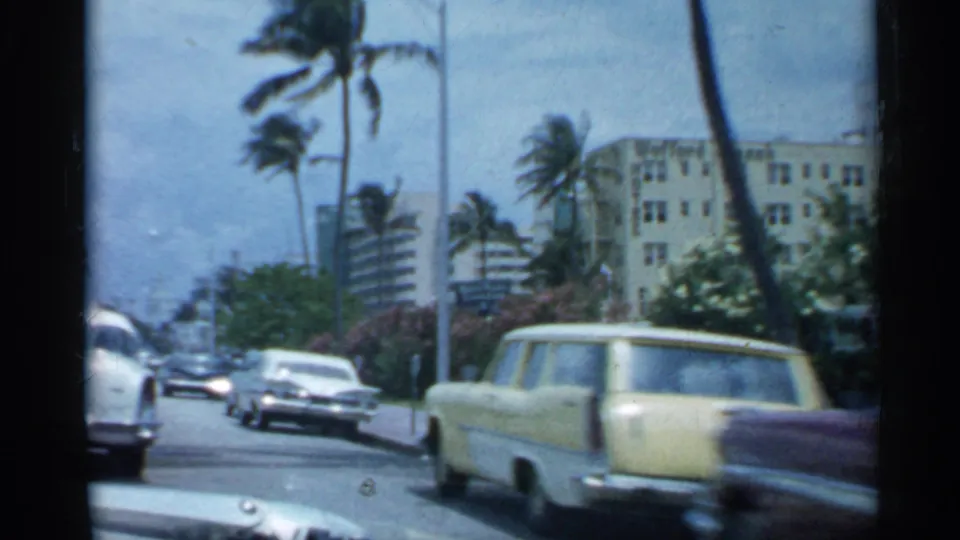 1958 Florida traffic scene with late-1950s cars, tall palms, roadside buildings, and a low curbside viewpoint from home-movie footage.