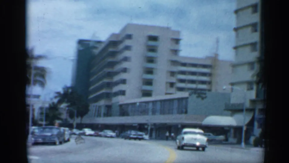 1958 Florida street view from a moving vehicle, showing classic cars, palms, and mid-century buildings along a broad urban road.