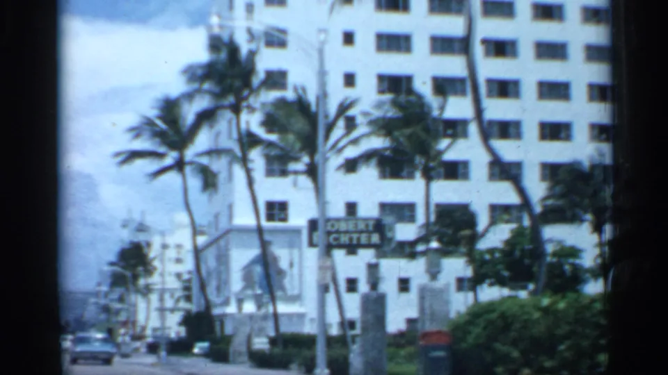 1958 Florida street scene with palm trees, cars, a white multi-story building, sidewalks, and a visible street sign near the curb.