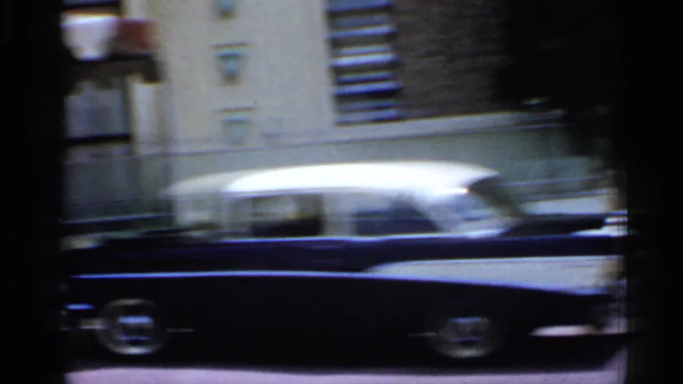A two-tone car streaks past a city building in the moving 1958 Florida home-movie street view.