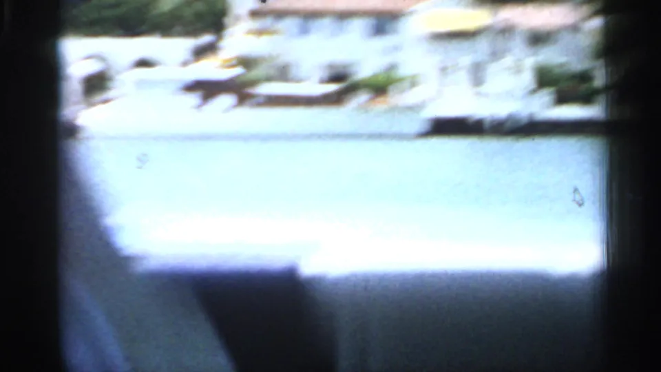 1958 Florida home-movie frame with a brief bright waterfront view and distant white buildings, partly obscured by dark scan edges.