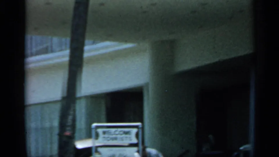 A Florida hotel frontage shows a palm trunk, balcony railings, shaded entrance, and a Welcome Tourists sign in 1958 8mm footage.