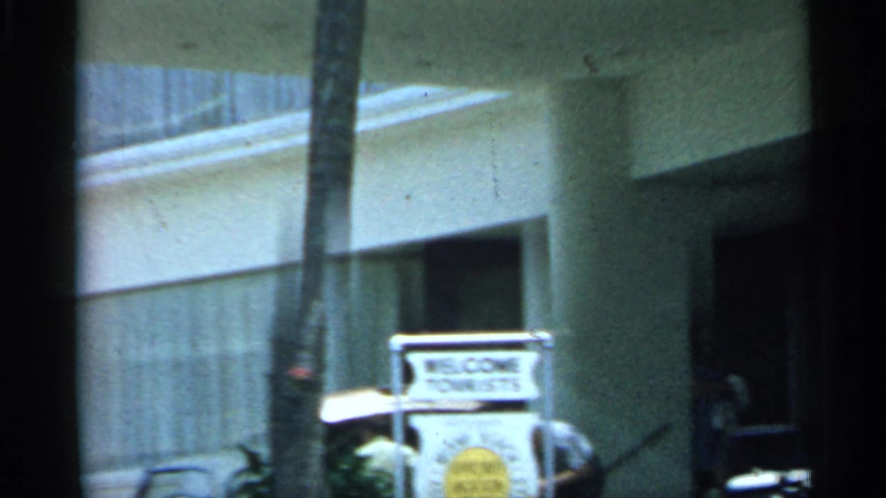 1958 Florida home-movie view of a tourist welcome sign near a white building, partially obscured by motion and film gate edges.