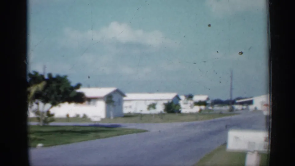 1958 Florida 8mm view of a quiet suburban street with white houses, lawns, trees, and a mailbox near the camera.