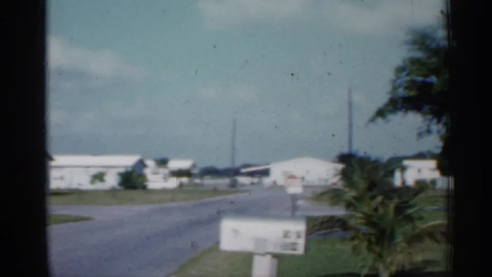 1958 Florida residential street scene with white houses, a paved road, palm foliage, lawns, and a roadside mailbox.