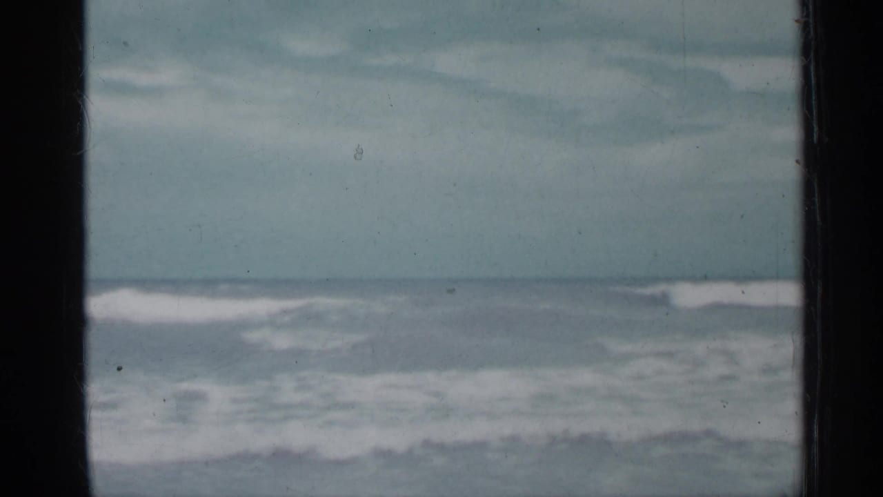 Ocean waves under a pale cloudy sky, seen between dark vertical frame edges.