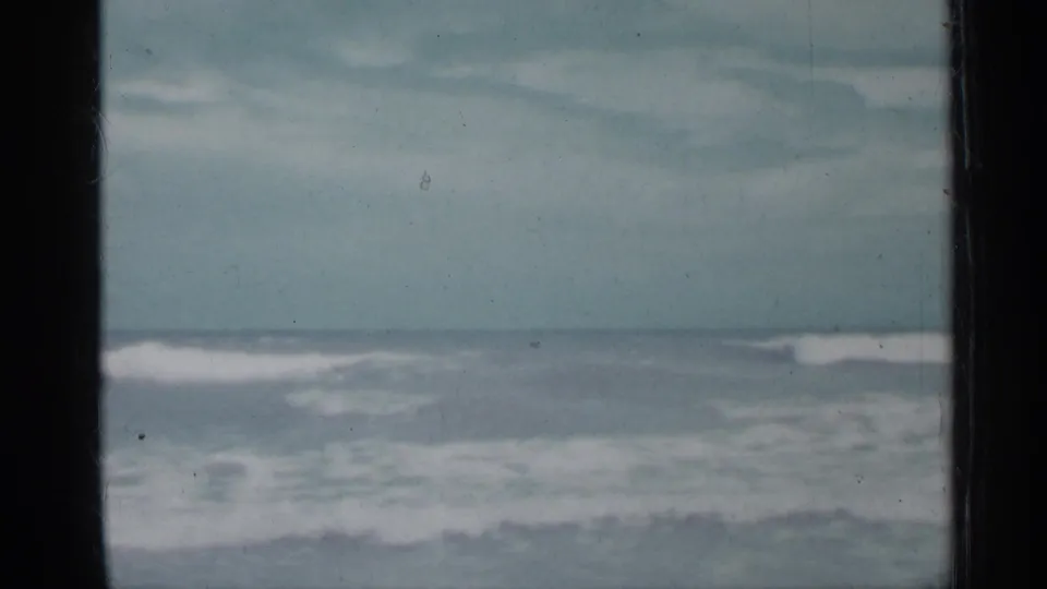 1958 Florida 8mm coastal view with shallow waves and white foam beneath a muted blue-gray sky, framed by dark vertical bars.