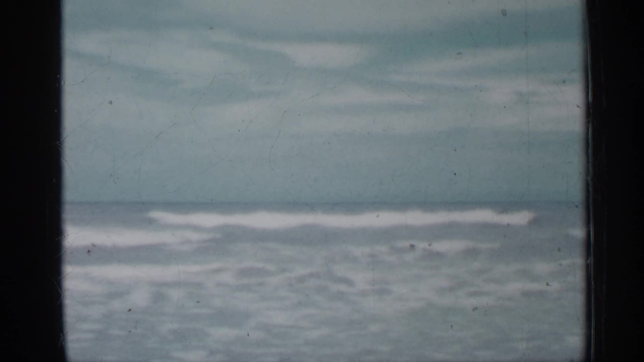 Muted 8mm view of Florida surf in 1958, with white wave crests, pale sky, and a dark vertical divider in the foreground.