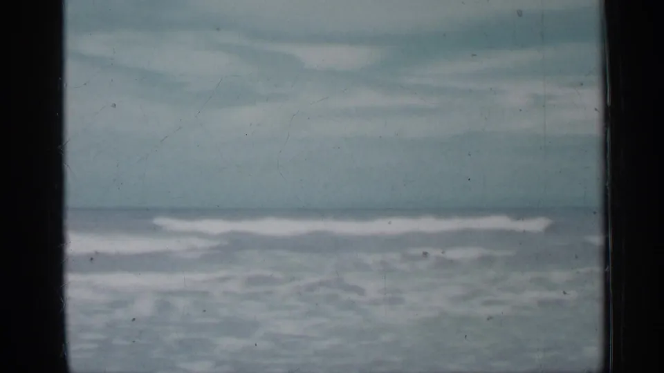 Muted 8mm view of Florida surf in 1958, with white wave crests, pale sky, and a dark vertical divider in the foreground.