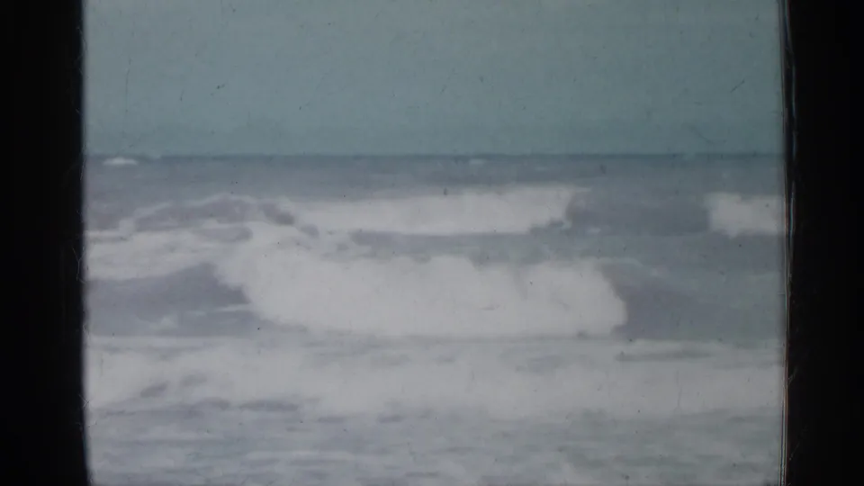 1958 Florida home-movie frame showing low ocean waves with white foam, a hazy horizon, and dark framing at the sides.