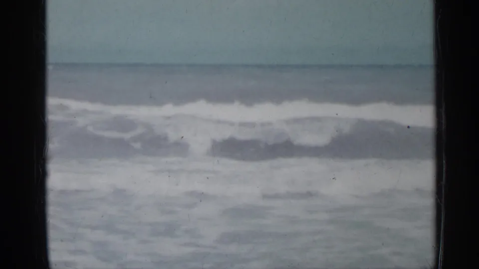 Florida coastal 8mm frame from 1958 with layered surf, white foam, muted sky, and a dark vertical divider along the left side.