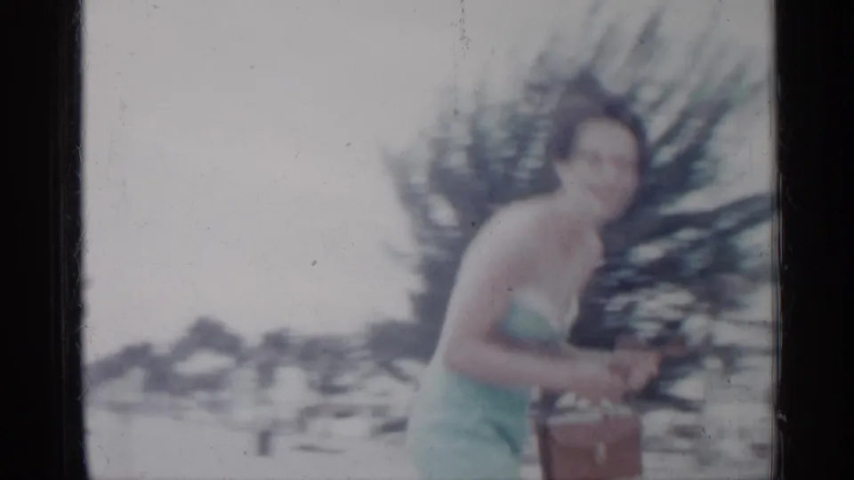 A closer, soft-focus 8mm frame shows the woman holding her brown handbag with trees and beach activity in the background.