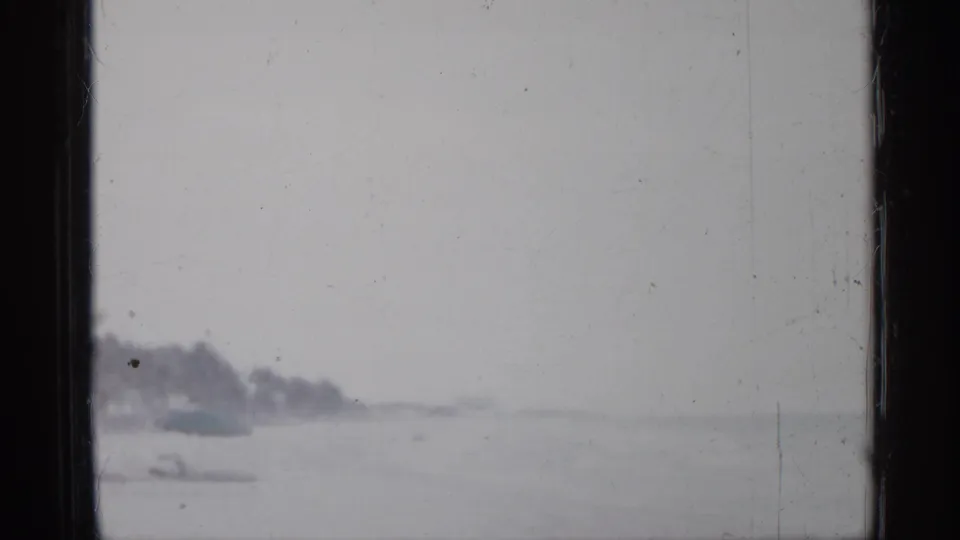 The final frame holds a pale, overexposed beach view with distant trees and shoreline after the woman has moved out of view.
