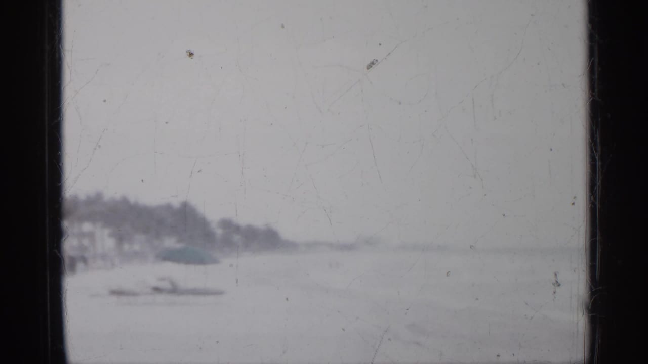 Distant coast and small boat seen through a scratched film frame.