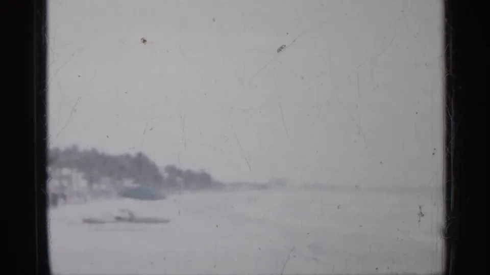 1958 Florida beach footage with a distant coastline, small boat shape, pale water, and heavy 8mm wear.