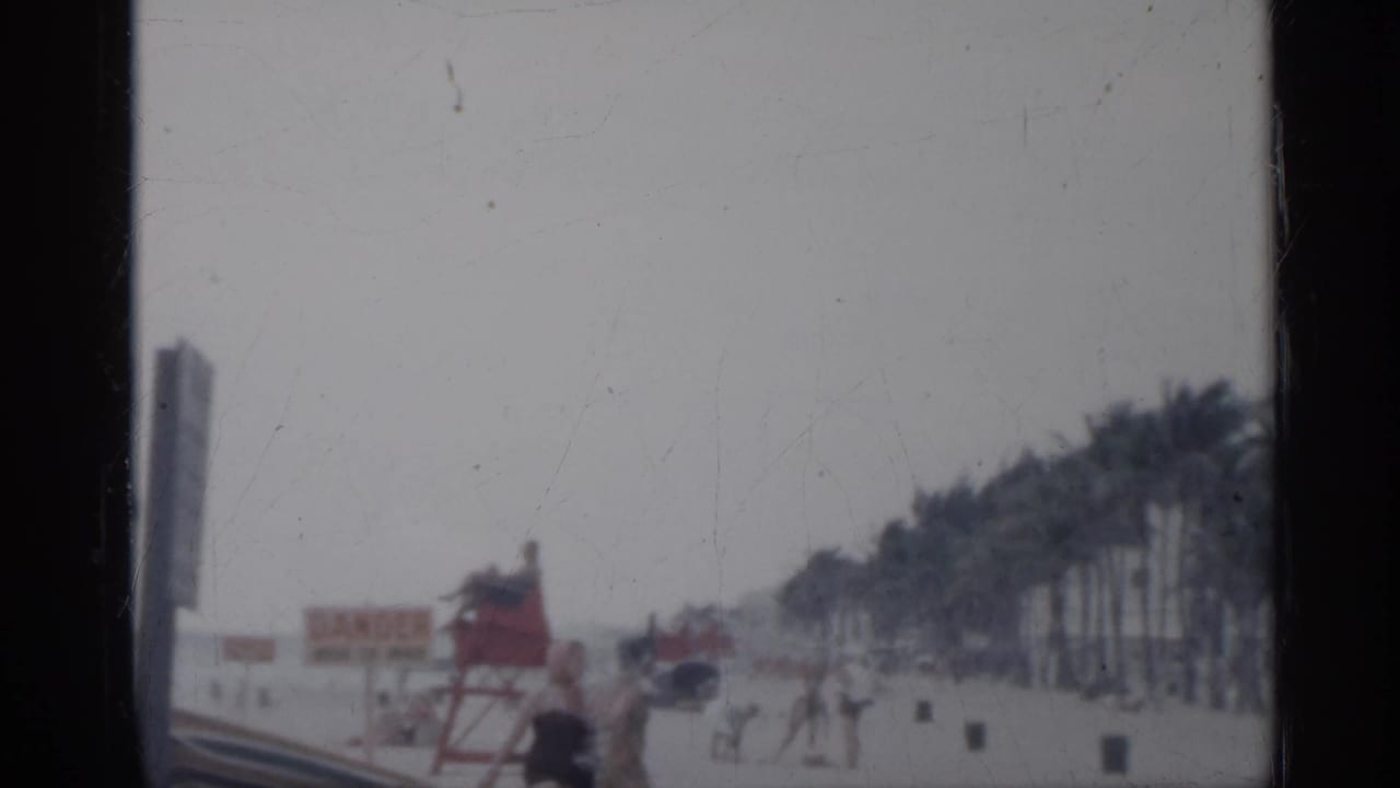 1958 Florida beach scene with a red lifeguard tower, warning signage, palm trees, and small distant figures on the sand.