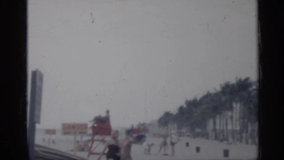 1958 Florida beach scene with a red lifeguard tower, warning signage, palm trees, and small distant figures on the sand.
