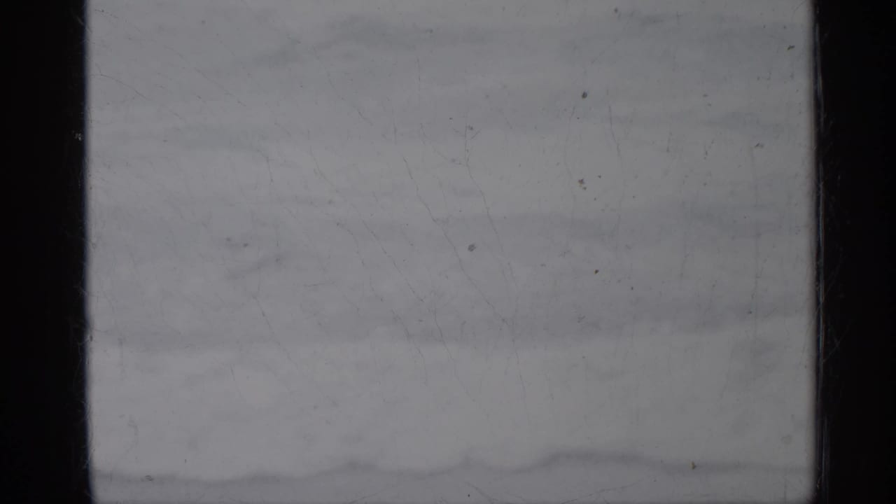 Overexposed 1958 Florida 8mm home-movie frame with dark gate edges, pale surface detail, dust, scratches, and no identifiable subject.