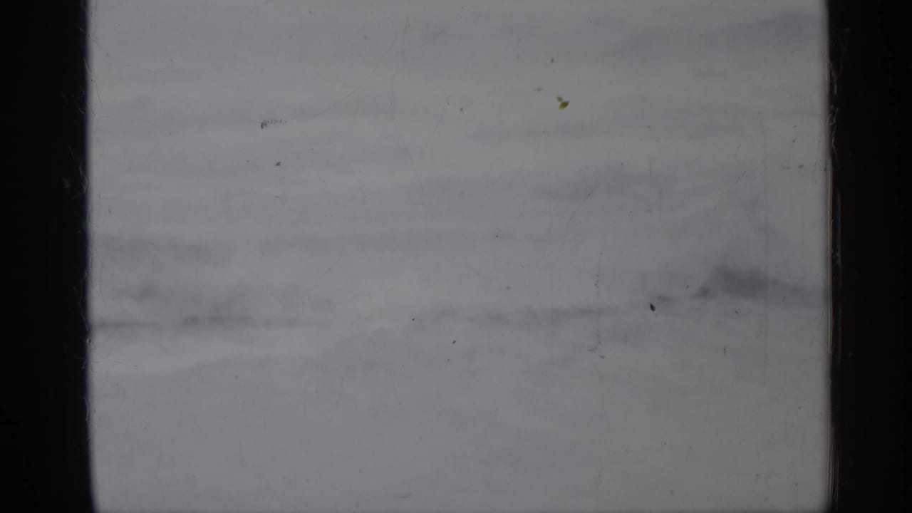 Pale blank frame with dark side border, faint banding, dust marks, and scratched film surface.