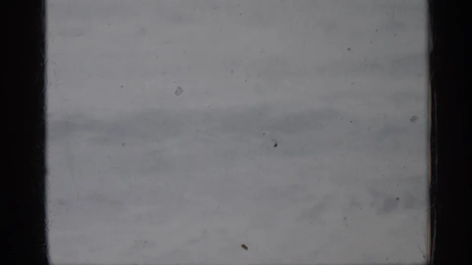 Blank-looking 8mm home-movie frame with a pale gray wash, dark film border, dust, scratches, and minimal visible scene information.