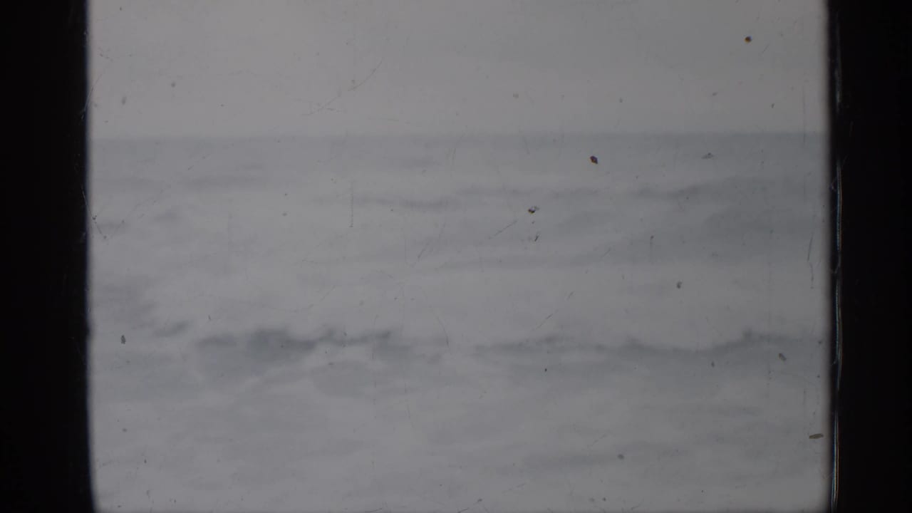 1958 Florida coastal view with rough gray water, pale overcast sky, film scratches, and dark vertical frame borders.