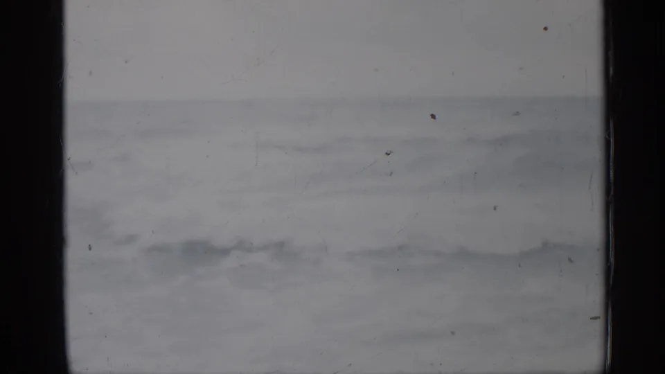 1958 Florida coastal view with rough gray water, pale overcast sky, film scratches, and dark vertical frame borders.