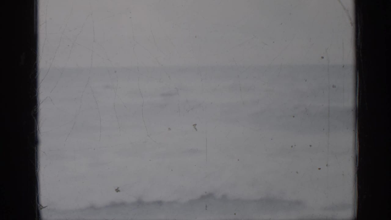 1958 Florida 8mm home-movie frame showing a muted seascape, low surf, pale horizon, and visible film wear at the gate edges.