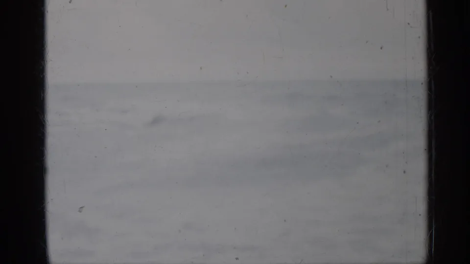 1958 Florida home-movie still of subdued surf and open water, with monochrome exposure, scratches, and dust visible on the film.