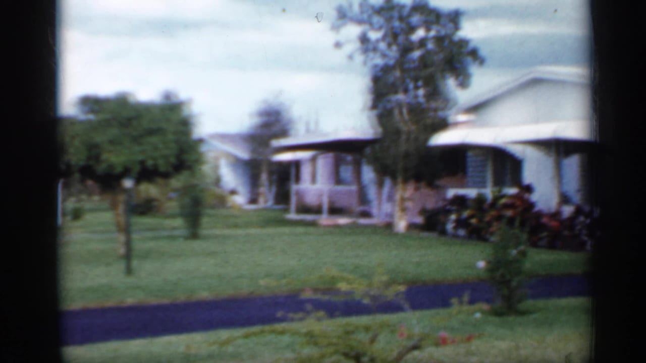 1958 Florida home-movie view of a manicured lawn with light-colored mobile homes and shrubs in the background.