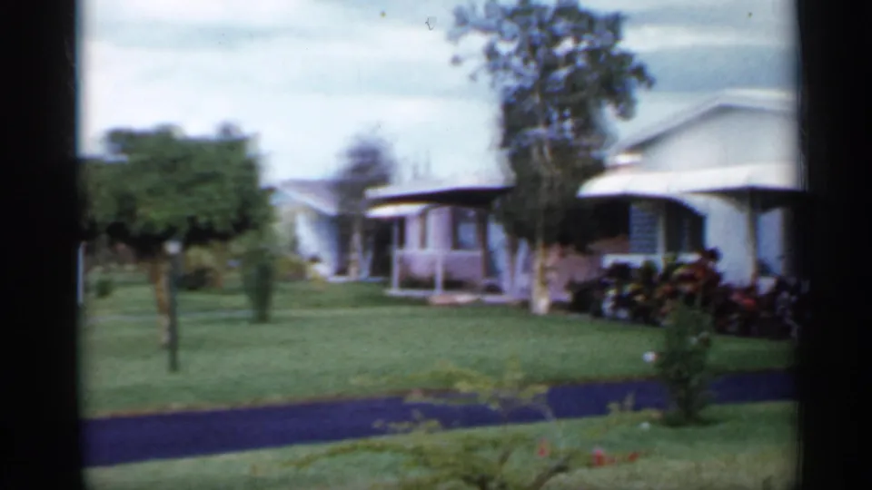 1958 Florida home-movie view of a manicured lawn with light-colored mobile homes and shrubs in the background.
