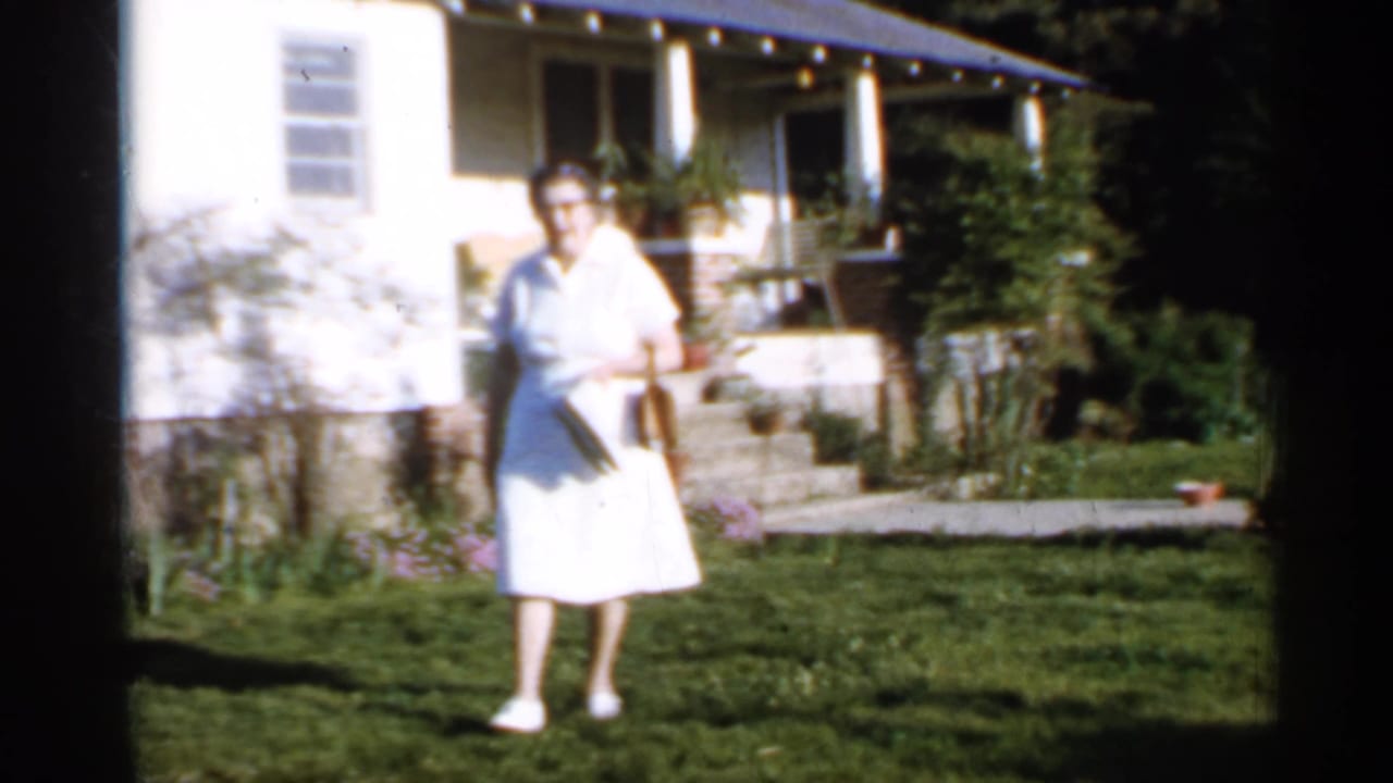 Woman in a white dress walking across a lawn in front of a house.
