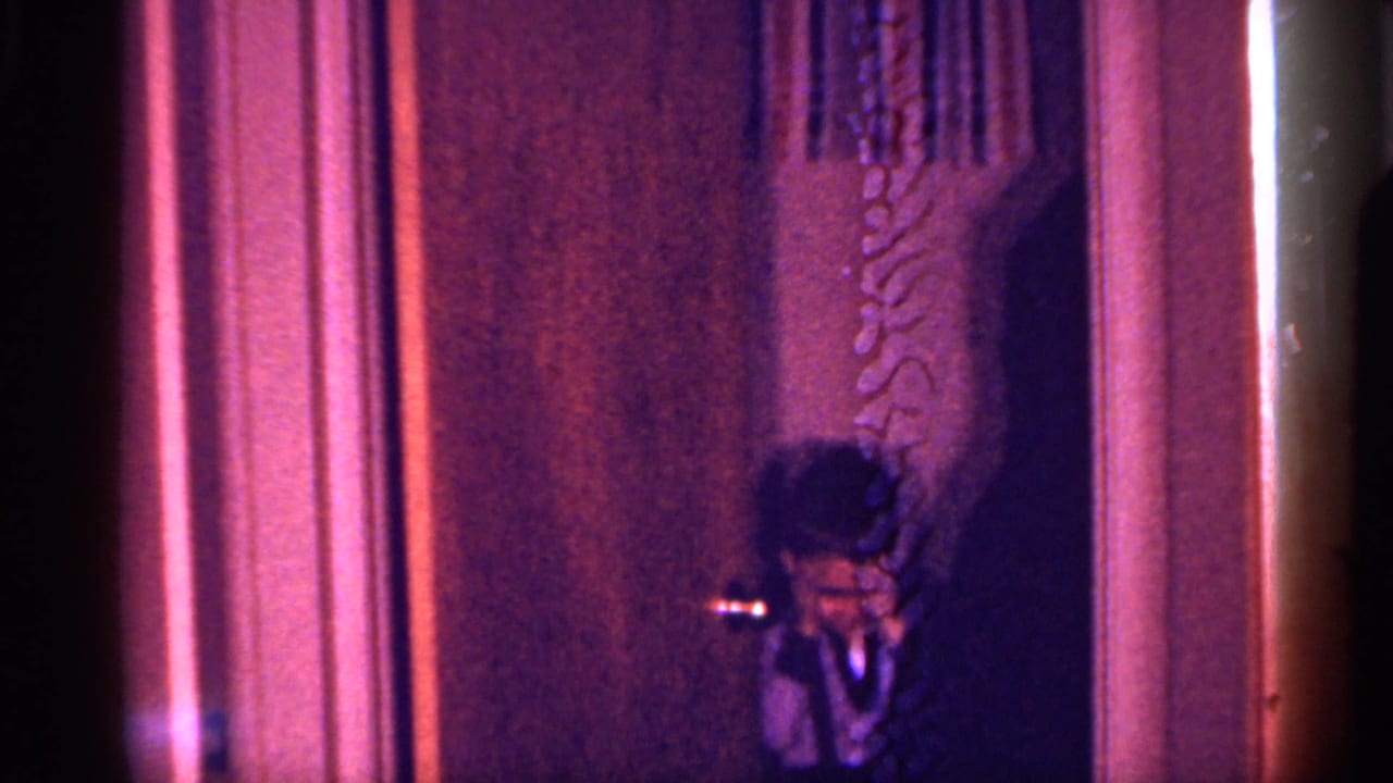 Dim interior doorway with a small figure partly visible beside curtains.