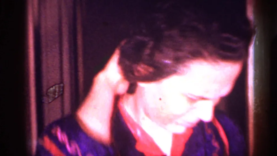 Close 1958 New Jersey home-movie view of the woman adjusting her hair, with strong exposure and color shift.