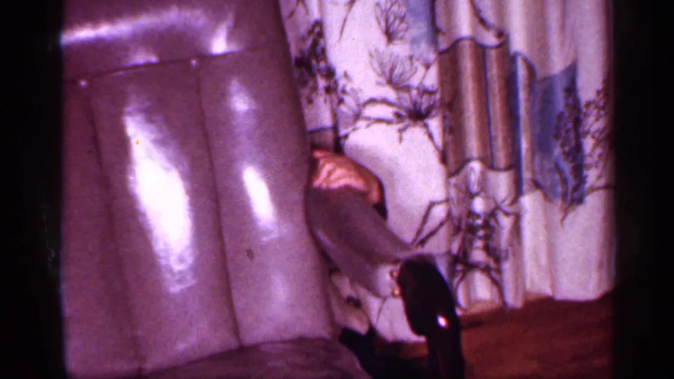 1958 New Jersey interior frame with the woman partly cropped near an upholstered chair and patterned curtains.