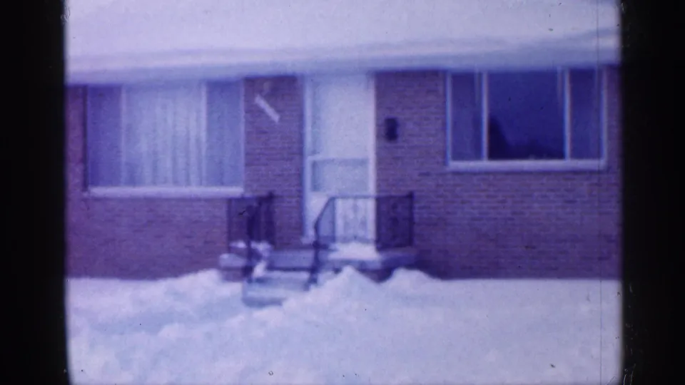 1958 New Jersey frame of a brick ranch-style house facade with front steps, railings, windows, and snow along the walkway.