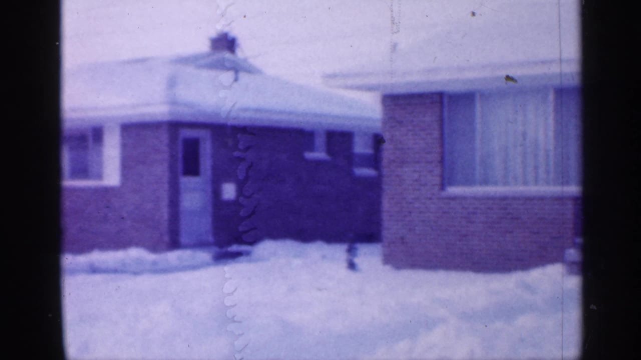 Snowy side view of brick house with door, window, and low roof.