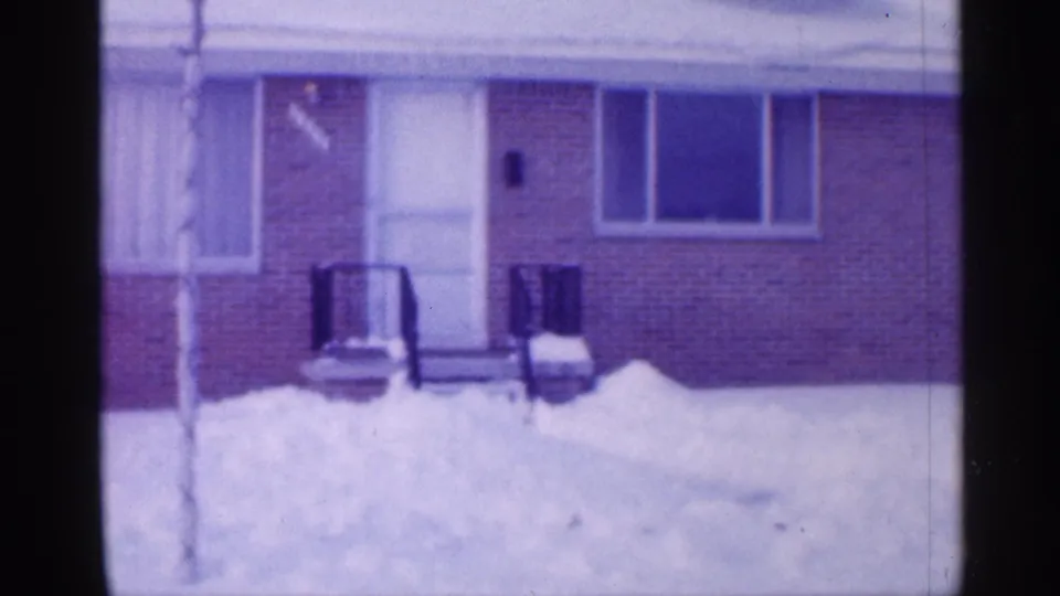1958 New Jersey home-movie view of a snow-covered front yard, porch railings, and large window on a small brick house.