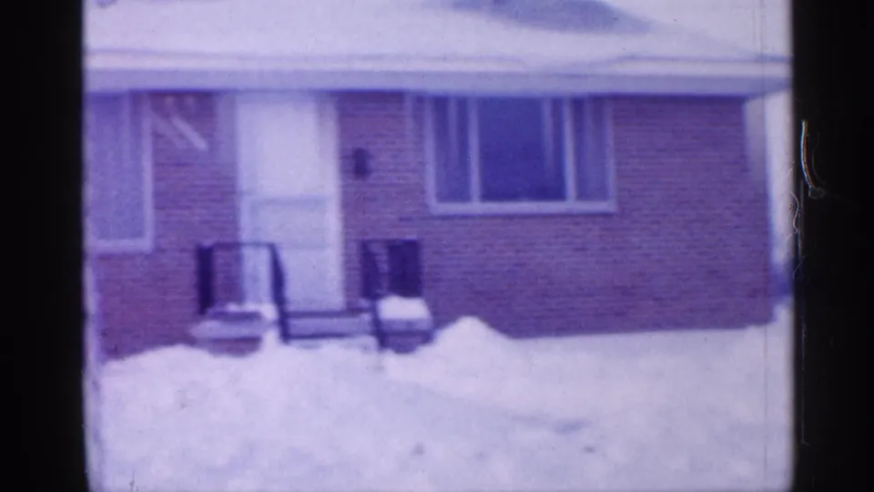 The camera pans to the brick house entrance, showing snow piled along the front, two chairs, windows, and a door in the 1958 New Jersey setting.