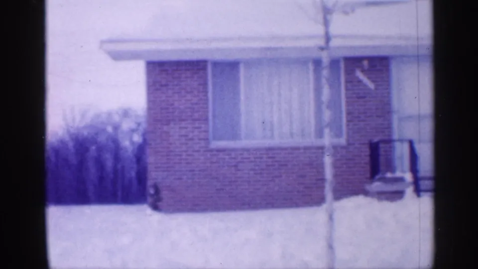 1958 New Jersey winter exterior with a brick home corner, curtained window, porch railing, and snow piled across the yard.
