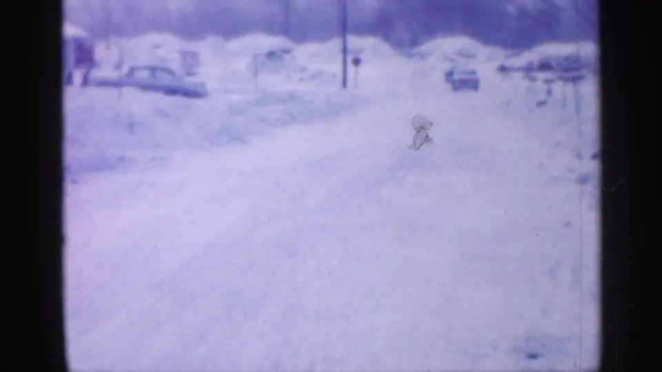 1958 New Jersey home-movie view down a snow-packed neighborhood road with distant houses, parked cars, and winter snowbanks.