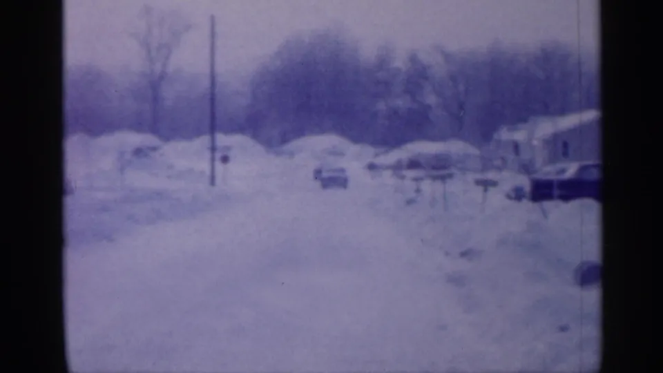 The frame shows a snowy 1958 New Jersey street with several parked cars, deep roadside snow, bare trees, and a house partly visible at right.