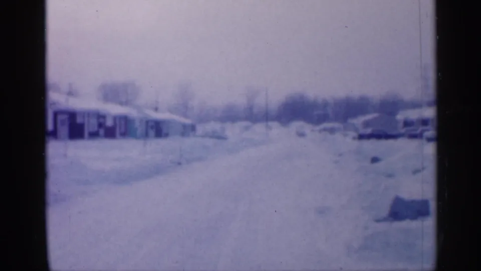 Final 1958 New Jersey frame shows a quiet residential road blanketed in snow, with houses to the left, cars to the right, and utility poles beyond.