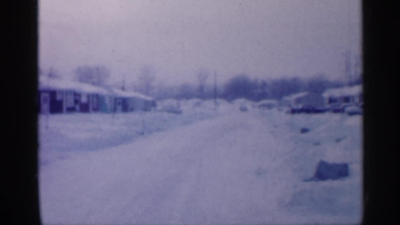 Snow-covered residential street with low homes and parked cars in soft focus.